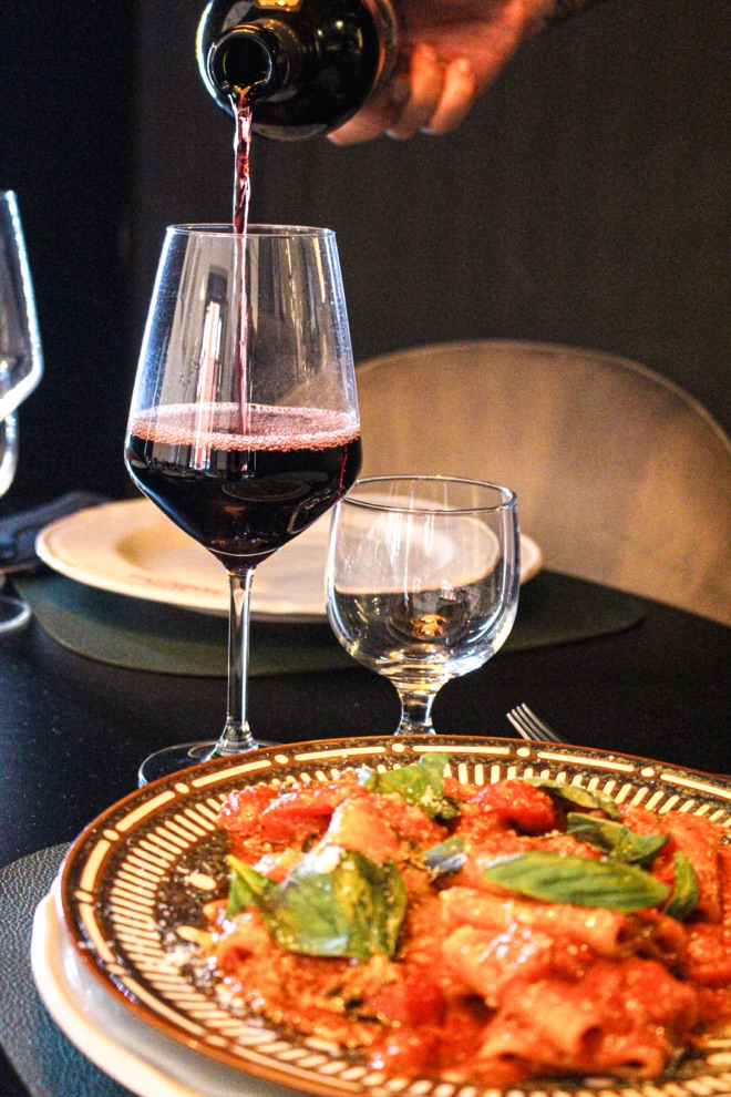 Vino rosso versato accanto a un piatto di pasta da Osteria Annunziata